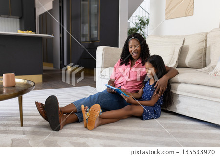 Mother and daughter sitting on floor using tablet, enjoying quality time together Mother and daughter sitting on floor using tablet, enjoying quality time together 135533970