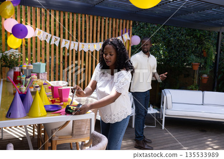 Preparing outdoor party table with colorful hats and balloons for celebration Preparing outdoor party table with colorful hats and balloons for celebration 135533989