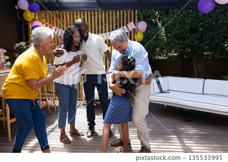 Celebrating birthday outdoors, grandfather hugging granddaughter, family smiling and clapping 135533995