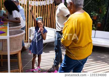 Young girl celebrating birthday with family outdoors, wearing party hat and smiling Young girl celebrating birthday with family outdoors, wearing party hat and smiling 135534000
