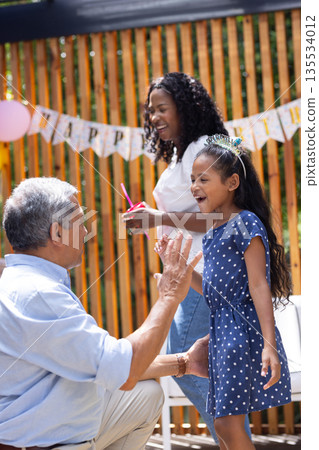 Grandfather playing with granddaughter, mother smiling at outdoor birthday party Grandfather playing with granddaughter, mother smiling at outdoor birthday party 135534012