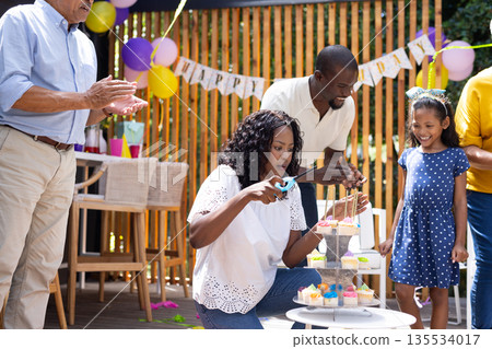 Celebrating birthday outdoors, family decorating cupcakes with colorful candles and balloons Celebrating birthday outdoors, family decorating cupcakes with colorful candles and balloons 135534017