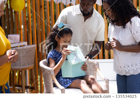 Celebrating birthday, African American family with child opening gift with excitement 135534025