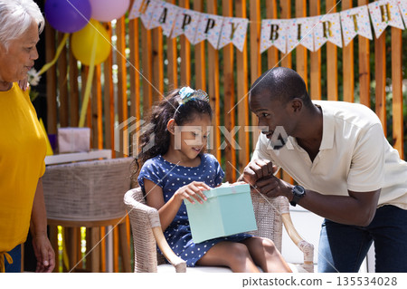 Grandfather and father celebrating birthday with excited girl opening gift outdoors Grandfather and father celebrating birthday with excited girl opening gift outdoors 135534028