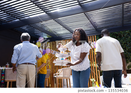 African American woman arranging dessert stand at family birthday party outdoors African American woman arranging dessert stand at family birthday party outdoors 135534036