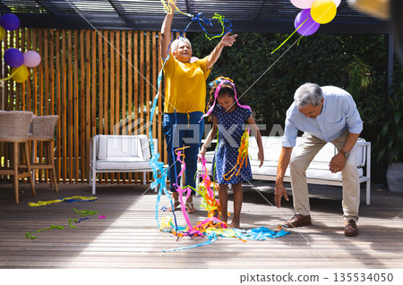Grandparents and granddaughter celebrating with colorful streamers on sunny patio Grandparents and granddaughter celebrating with colorful streamers on sunny patio 135534050