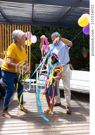 Grandparents and child playing with colorful streamers at outdoor family party 135534052