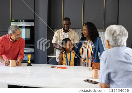 Celebrating child's achievement, family smiling together in kitchen, feeling proud 135534066