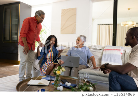 Family enjoying conversation at home, smiling and using laptop together on couch 135534069