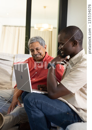 Grandfather and grandson using laptop together at home, sharing joyful moment 135534076