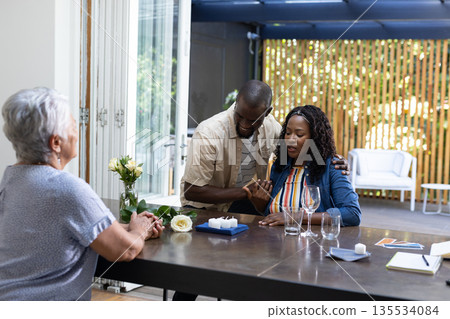 Sharing news, African American couple with elderly woman at dining table, emotional Sharing news, African American couple with elderly woman at dining table, emotional 135534084