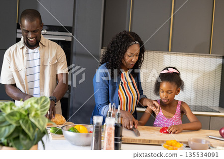 Family cooking together in modern kitchen, smiling and preparing fresh vegetables 135534091