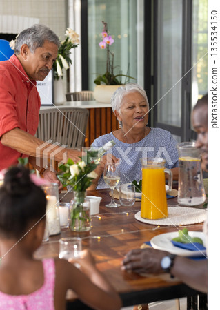 Family sharing meal at home, laughing and conversing around dining table 135534150