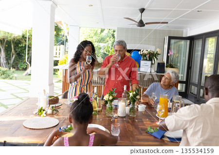 Smiling warmly, African American family sharing drinks at outdoor dining table Smiling warmly, African American family sharing drinks at outdoor dining table 135534159