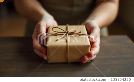A person holds a wrapped gift box on a table, symbolizing kindness and generosity on World Kindness Day A person holds a wrapped gift box on a table, symbolizing kindness and generosity on World Kindness Day 135534230