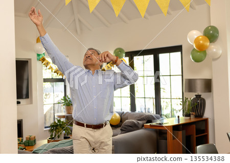 Middle-aged man adjusting yellow pennant banner in living room, with green balloons Middle-aged man adjusting yellow pennant banner in living room, with green balloons 135534388