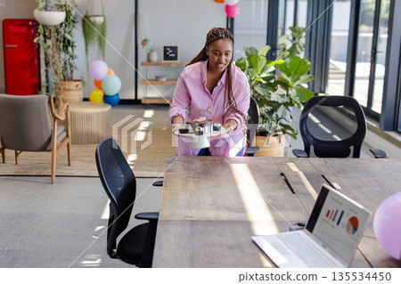 African American woman walking to conference table at office holding birthday cake with lit candles African American woman walking to conference table at office holding birthday cake with lit candles 135534450