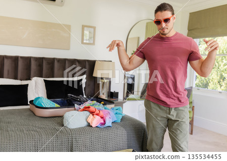 Young adult woman packing colorful clothes into open suitcase on bed in modern bedroom, copy space Young adult woman packing colorful clothes into open suitcase on bed in modern bedroom, copy space 135534455