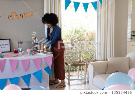 African American woman arranging cupcakes on cupcake stand in living room with bunting, copy space African American woman arranging cupcakes on cupcake stand in living room with bunting, copy space 135534456