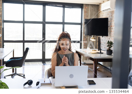 Woman sitting at white desk in modern loft office, using silver laptop with headphones Woman sitting at white desk in modern loft office, using silver laptop with headphones 135534464