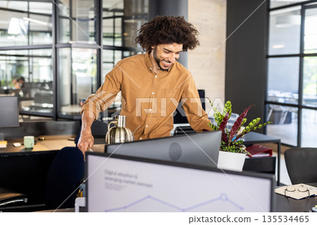 Asian man working on line graph at bright modern open-plan office, with coffee carafe and planter Asian man working on line graph at bright modern open-plan office, with coffee carafe and planter 135534465