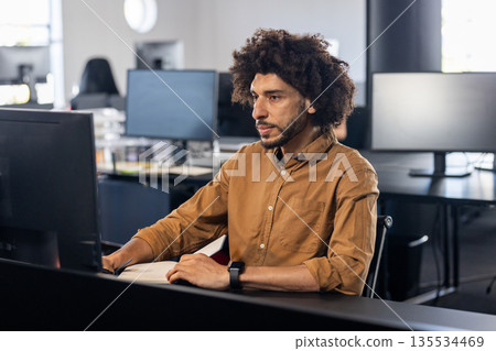 Young adult Asian man typing code at desk in open?plan office, with computer monitor and smartwatch Young adult Asian man typing code at desk in open?plan office, with computer monitor and smartwatch 135534469
