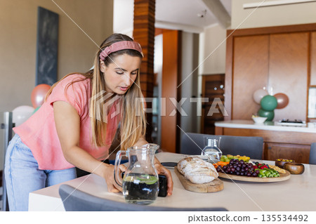 Woman photographing cutting board with bread and grapes using smartphone in kitchen, copy space Woman photographing cutting board with bread and grapes using smartphone in kitchen, copy space 135534492