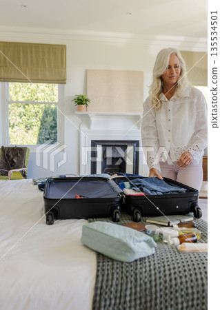 Senior woman packing black suitcase in bright bedroom, with toiletry bag and passport, copy space Senior woman packing black suitcase in bright bedroom, with toiletry bag and passport, copy space 135534501
