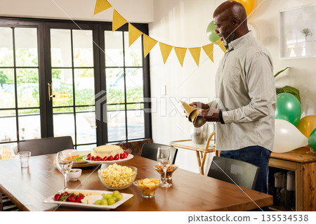 African American senior man holding party hats in dining room at home, with balloons, copy space 135534538