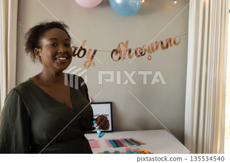 Smiling African American woman holding party popper at baby shower with gold banner and balloons Smiling African American woman holding party popper at baby shower with gold banner and balloons 135534540