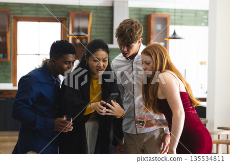 Teenagers gathering around smartphone, sharing exciting news at home celebration Teenagers gathering around smartphone, sharing exciting news at home celebration 135534811