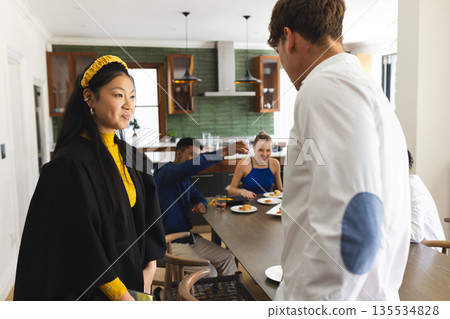 Asian girl in graduation gown celebrating with friends at home, smiling and talking 135534828