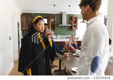 Teens in graduation gowns celebrating with drinks at home, enjoying moment Teens in graduation gowns celebrating with drinks at home, enjoying moment 135534829