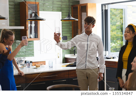 Teen friends celebrating at home, raising glasses and smiling in kitchen 135534847