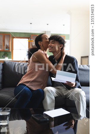 Celebrating on couch, African American mother hugging teenage son holding letter Celebrating on couch, African American mother hugging teenage son holding letter 135534853