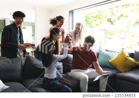 Teen friends celebrating success at home, high-fiving and smiling on couch Teen friends celebrating success at home, high-fiving and smiling on couch 135534855