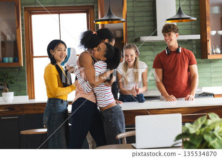 In kitchen, teens hugging and laughing with friends, celebrating togetherness 135534870