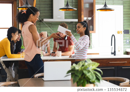 Teen sharing card with friends in kitchen, enjoying cheerful celebration together 135534872