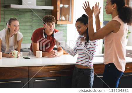 Teens celebrating good news in kitchen, reading letter with excitement and joy Teens celebrating good news in kitchen, reading letter with excitement and joy 135534881