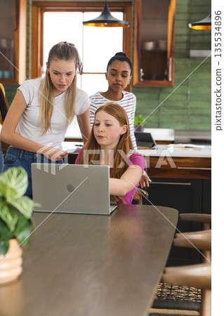Teen girls collaborating on laptop project in modern kitchen setting Teen girls collaborating on laptop project in modern kitchen setting 135534896