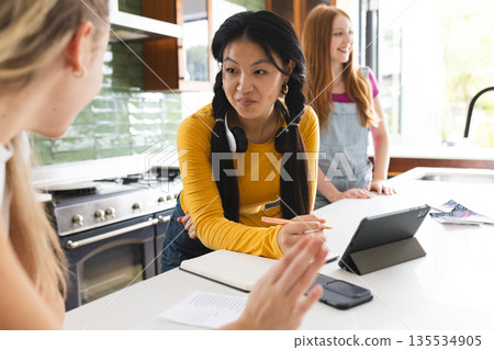 Asian girl with headphones smiling and talking with friends in modern kitchen Asian girl with headphones smiling and talking with friends in modern kitchen 135534905