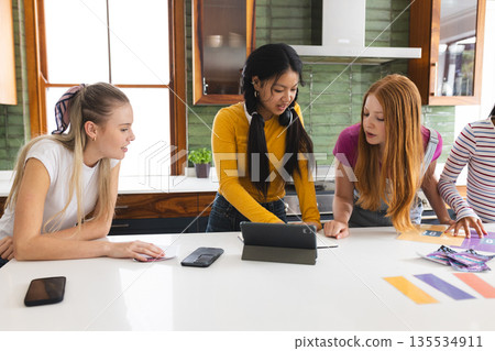 Teen girls collaborating on school project using tablet in modern kitchen 135534911