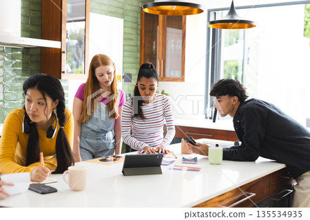 Teens collaborating on school project using tablet and smartphones in modern kitchen Teens collaborating on school project using tablet and smartphones in modern kitchen 135534935