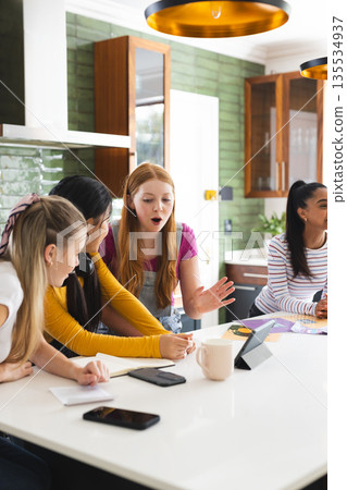 Teen girls excitedly discussing project at home, using tablet and notebooks Teen girls excitedly discussing project at home, using tablet and notebooks 135534937