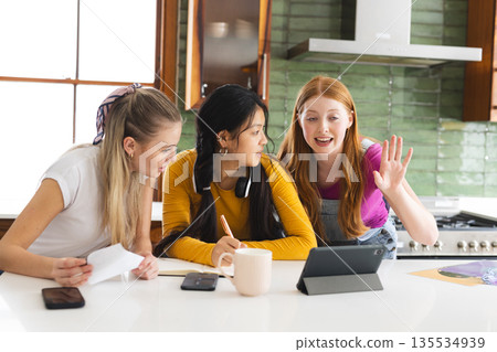 Teen girls studying together in kitchen, using tablet and taking notes Teen girls studying together in kitchen, using tablet and taking notes 135534939
