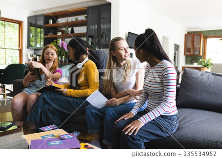 Teen girls sitting on couch at home, sharing notes and enjoying conversation Teen girls sitting on couch at home, sharing notes and enjoying conversation 135534952