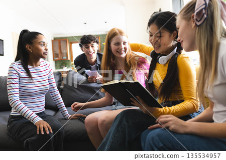 Teens laughing and reading book together on couch, enjoying group study session Teens laughing and reading book together on couch, enjoying group study session 135534957