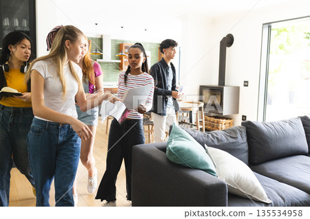 Teen friends discussing project while holding papers in modern living room 135534958