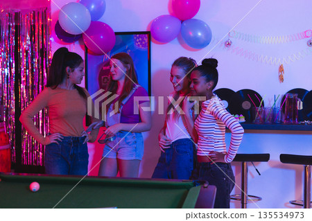 Teen girls enjoying party together, chatting and laughing near pool table 135534973