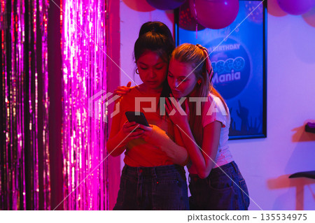 Teen girls sharing moment while looking at smartphone during birthday party 135534975